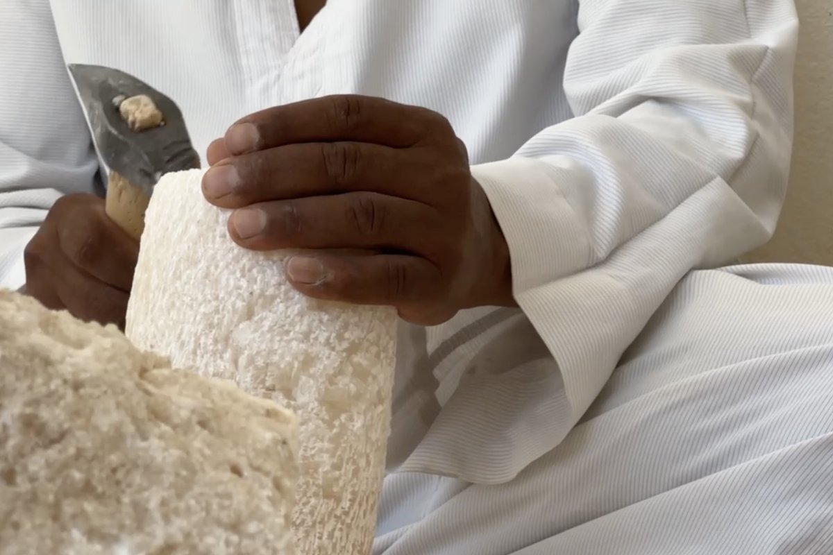 Craftsman's hands shaping a rough alabaster block with a chisel