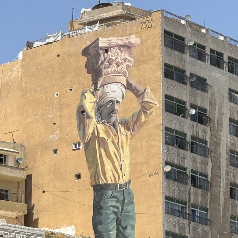 Large street mural of a figure carrying a Corinthian column capital, Amman